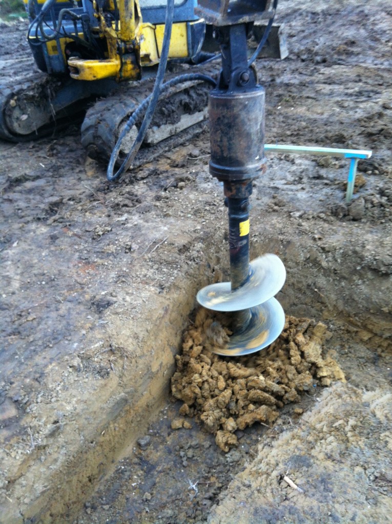 Using the auger to bore the piers beneath the strip footing