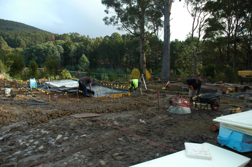 Steve and Greg laying the plastic sheet for the concrete to be poured over; Pete using the wheelbarrows as a makeshift sawhorse 