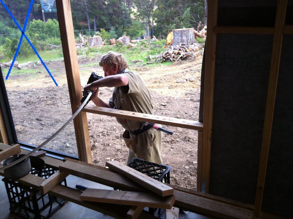 Easy in: greg installs the bedroom window. The blue cross is tape over the window to prevent anybody thinking it is open and chucking an offcut piece of timber through it.